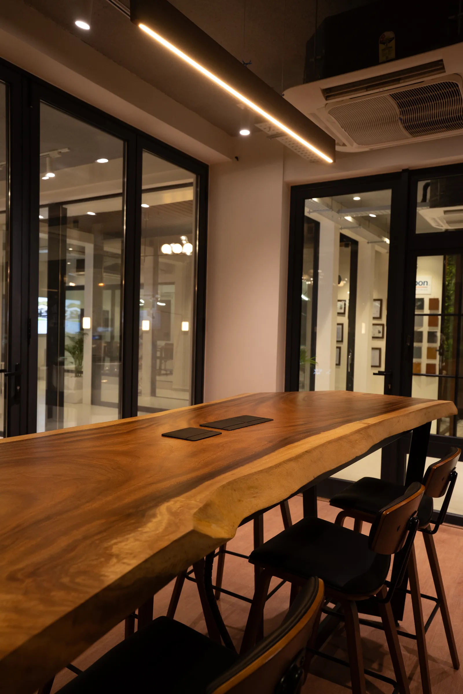 Wooden live-edge table with aluminium door displays behind — Aluk Experience Center